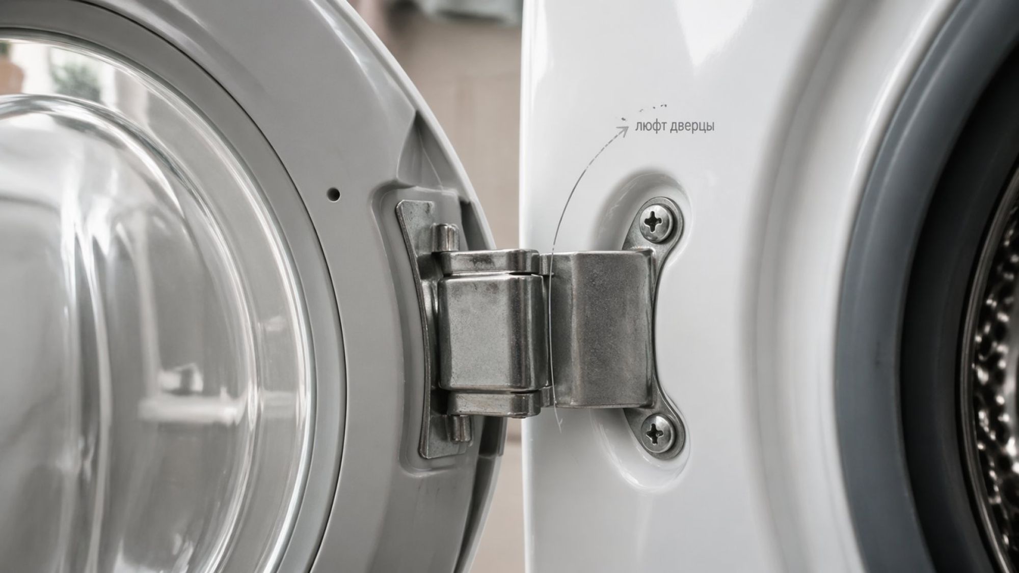 Крупный план люка фронтальной стиральной машины, дверца полностью открыта влево. Справа виден кусок белого корпуса, слева — прозрачное стекло люка. В центре кадра крупно показана